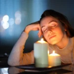 Woman relaxing beside lit candles creating a warm and calming fragrance ambiance