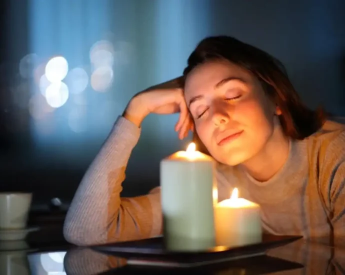 Woman relaxing beside lit candles creating a warm and calming fragrance ambiance